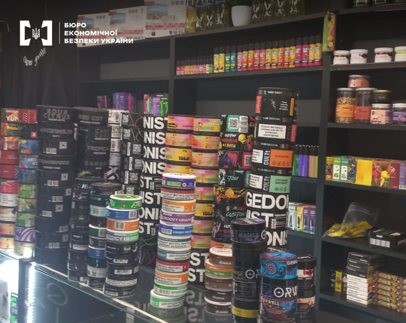 Вітрина та прилавок магазину  заставлені різноманітними банками та пачками тютюнових виробів, сумішей для куріння кальяну та вейпінгу.