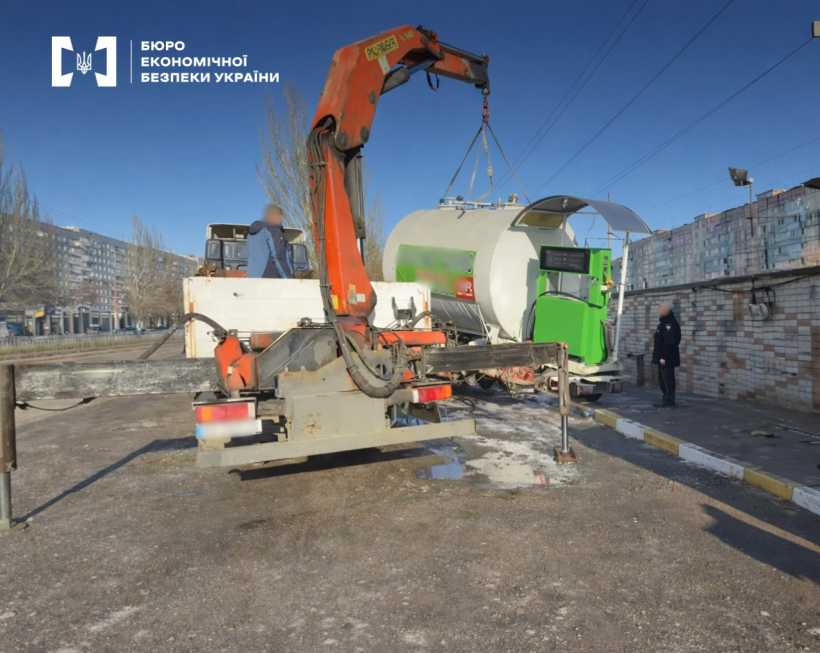 Демонтаж обладнання нелегальної АЗС за допомогою вантажного автомобіля з гідроманіпулятором (краном). На тлі міські будівлі та блакитне небо.