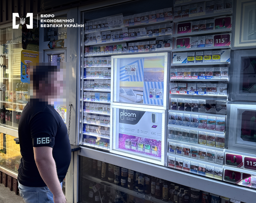 Детектив БЕБ оглядає скляну вітрину із широким асортиментом тютюнової продукції та рекламою електронних сигарет.