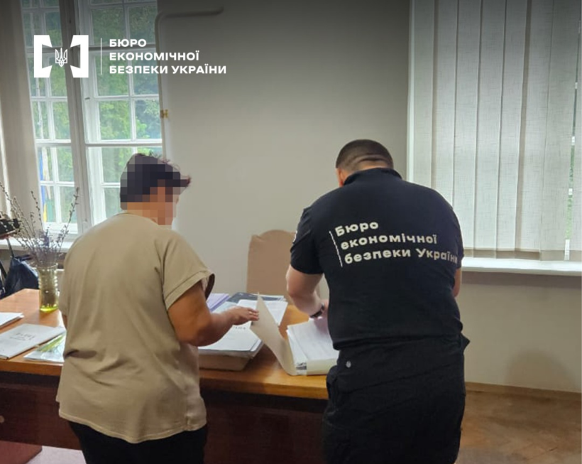 Слідчі дії в робочому кабінеті. Детектив БЕБ оглядає документи. Ліворуч жінка, обличчя заблюрено.