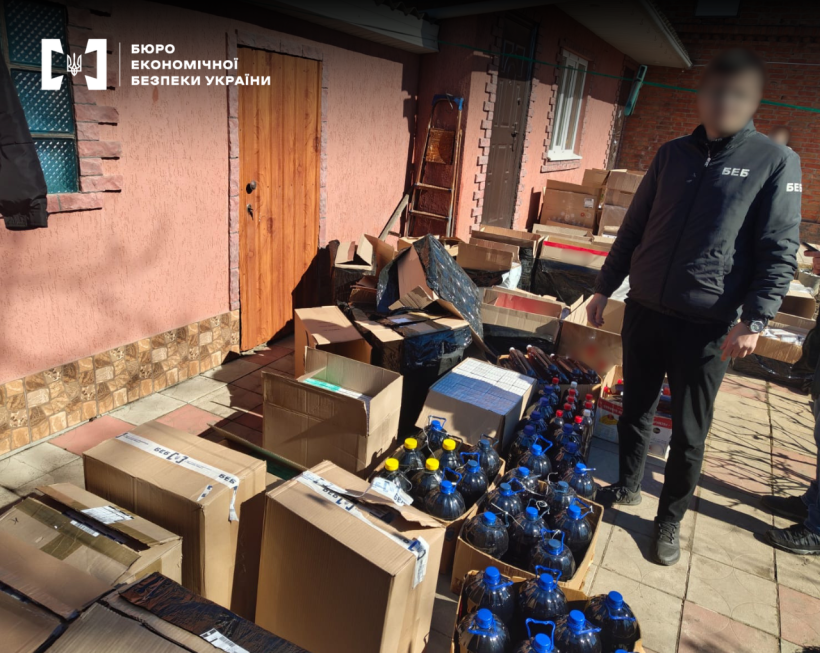 Детектив БЕБ на подвір’ї приватного будинку поруч із численними коробками контрафактного алкоголю та сигарет.