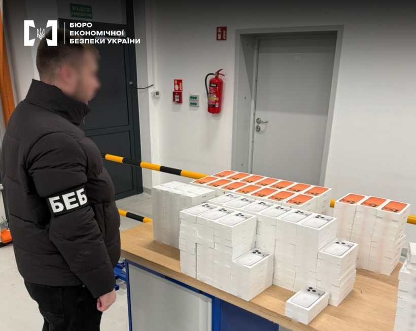 Детектив БЕБ оглядає велику партію вилучених смартфонів Apple у коробках.