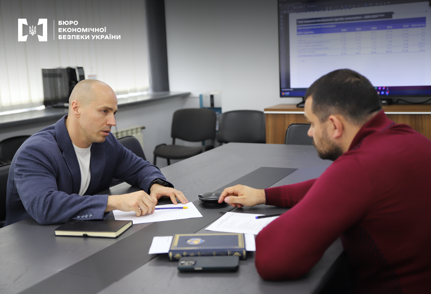 Керівник детективів БЕБ Олександр Ткачук з представником KPMG дискутують за офісним столом. На столі документи, записники. На екрані на стіні таблиця.