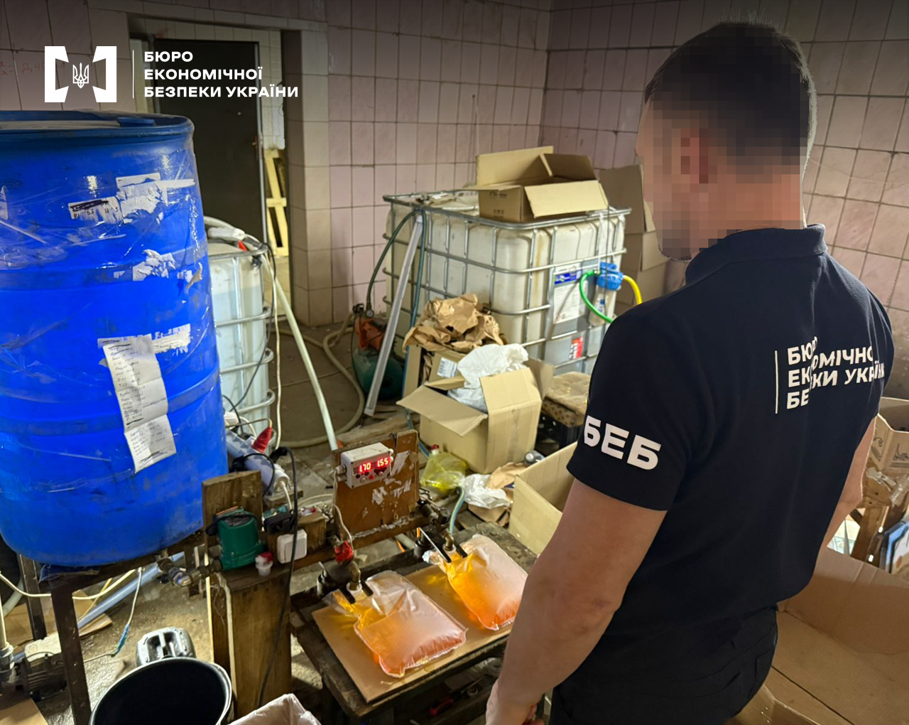 Детектив БЕБ оглядає саморобне обладнання для розливу алкоголю у тетрапаки у підпільному цеху з виробництва контрафакту.