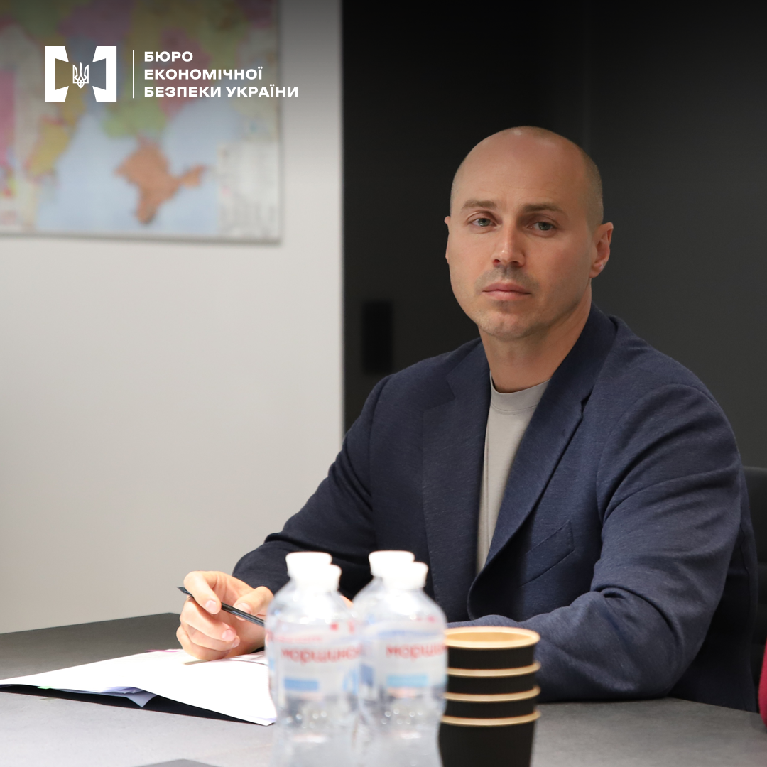 Керівник детективів БЕБ Олександр Ткачук під час зустрічі у конференц-залі. На столі записник, вода в ПЕТ плашках, стакани. На стіні карта світу. 
