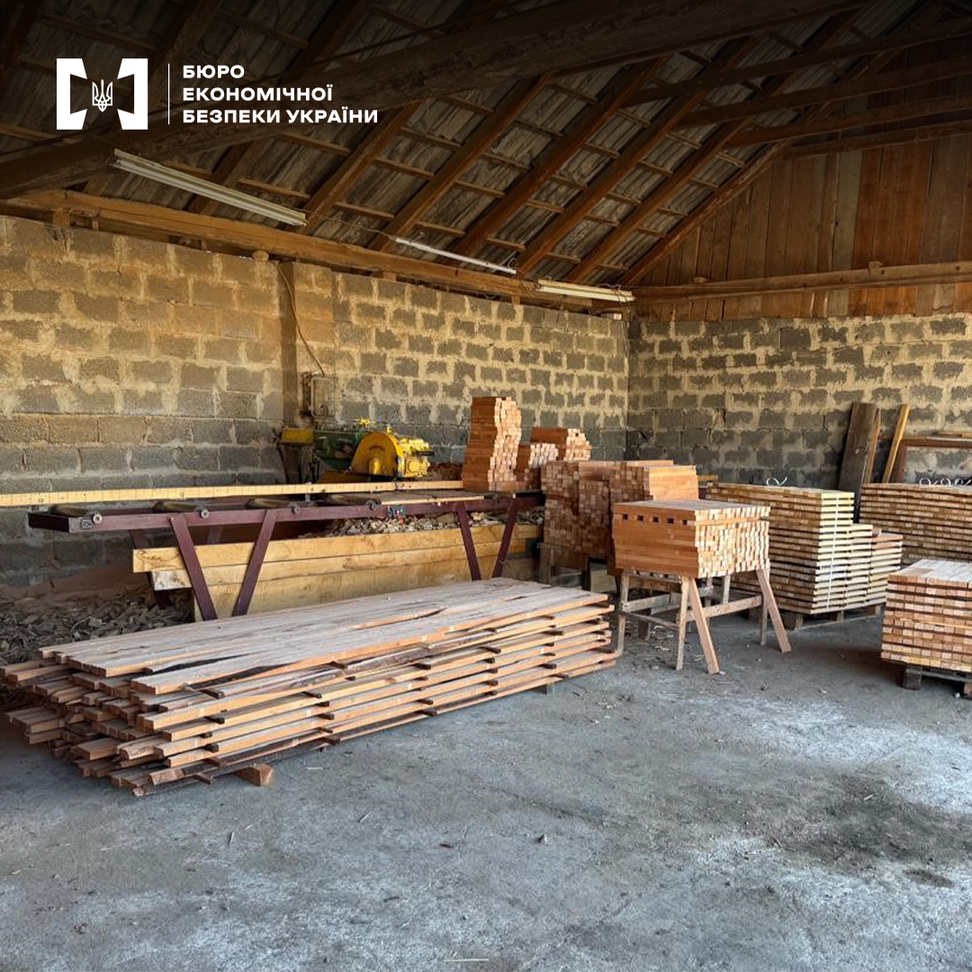 Деревообробна майстерня з цегляними стінами. Штабелі пиломатеріалів, робочий стіл, верстат та інструменти.