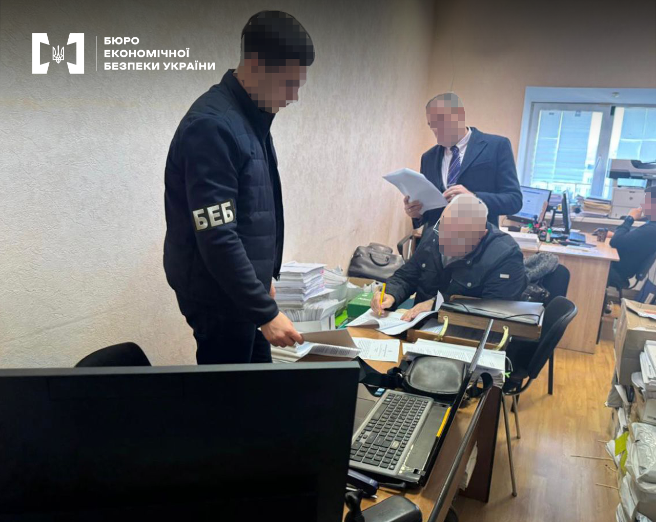 Детектив БЕБ вручає підозру фігуранту справи. Офісне приміщення. Робочі місця з документами та комп’ютерною технікою, працівники за роботою.