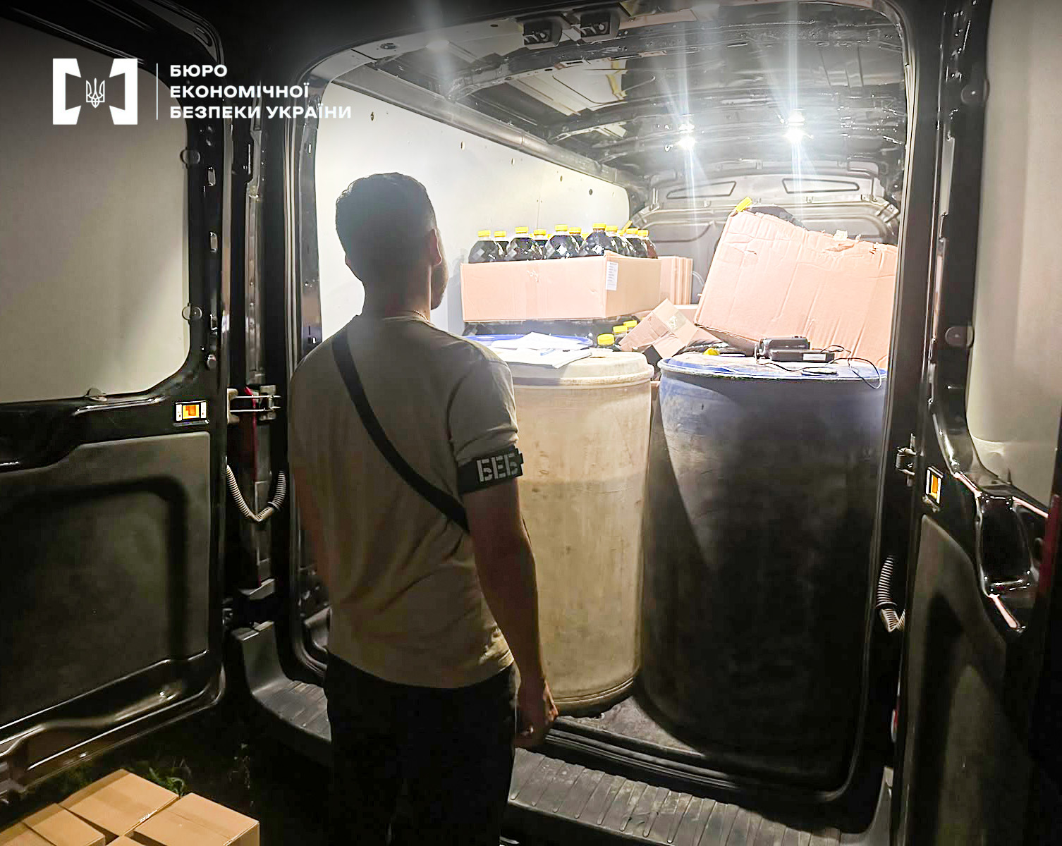 A ESBU detective inspects the body of a van with seized large barrels and bottles.