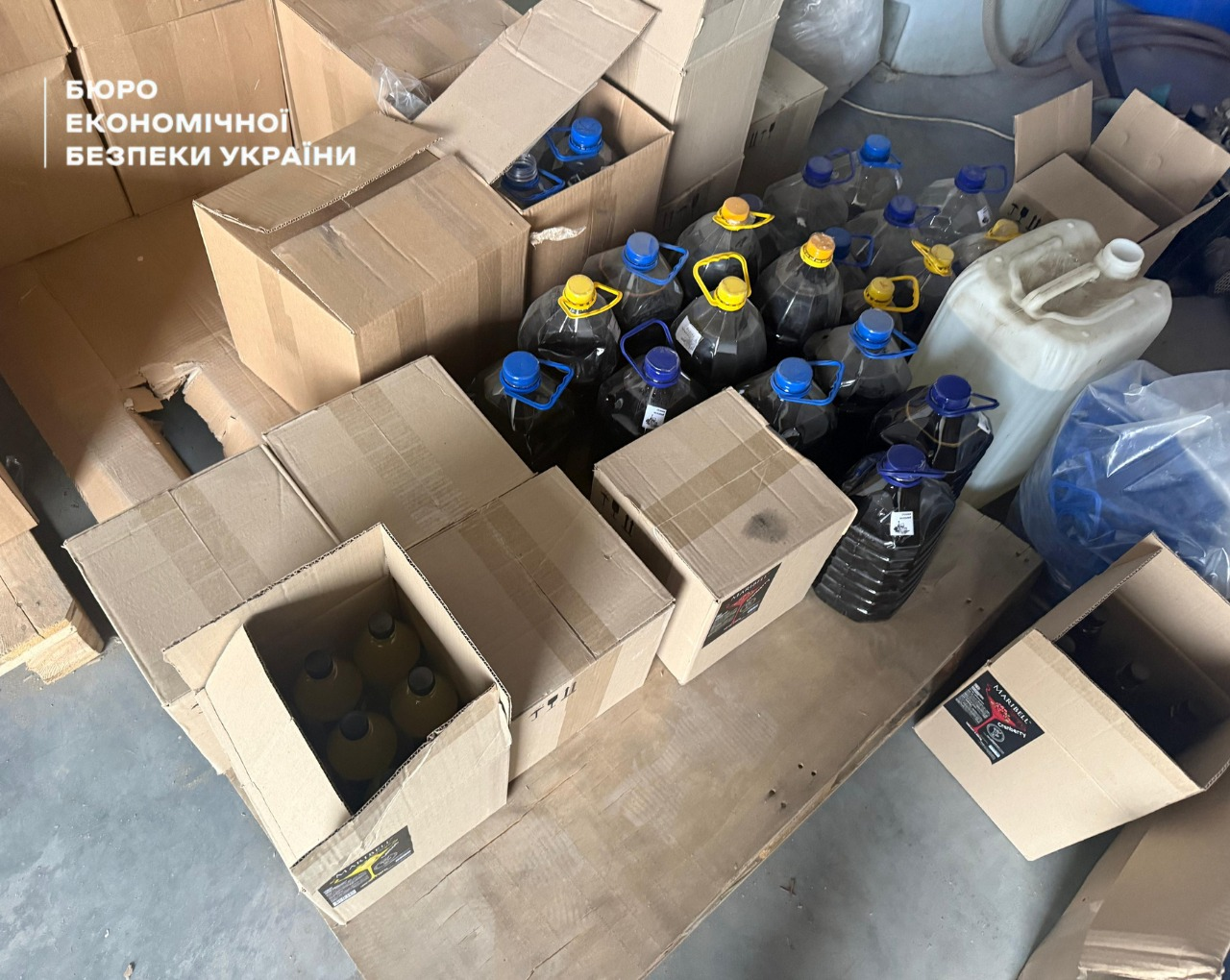 Large cardboard boxes with bottles, dark 5-liter plastic bottles, and white canisters on a wooden pallet. 