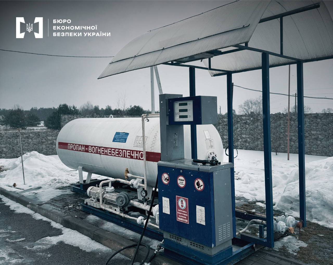 A gas station in winter: a white tank with a hazard warning sign and a fuel dispenser.