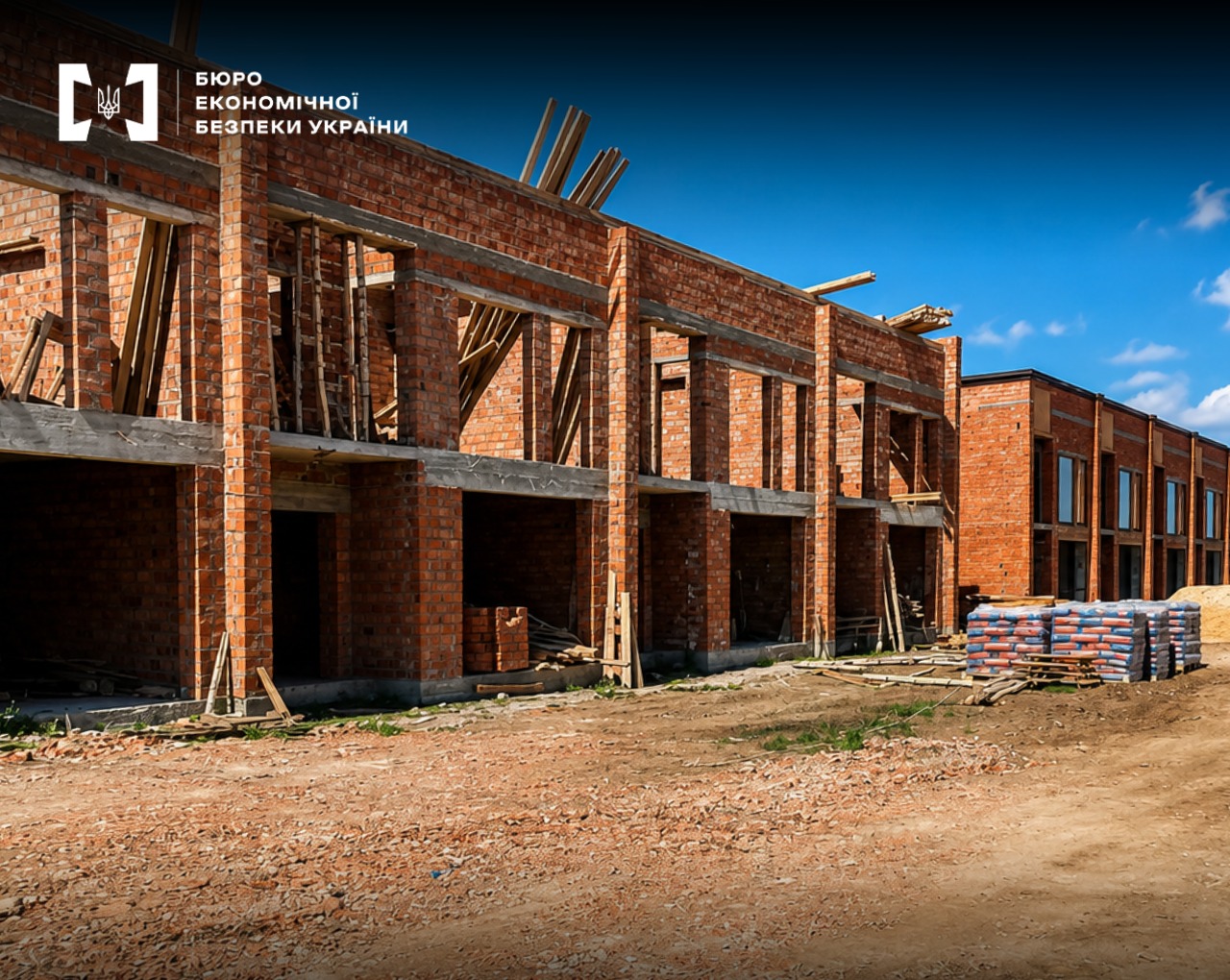 A construction site of a two-story red-brick townhouse against the backdrop of a clear blue sky.