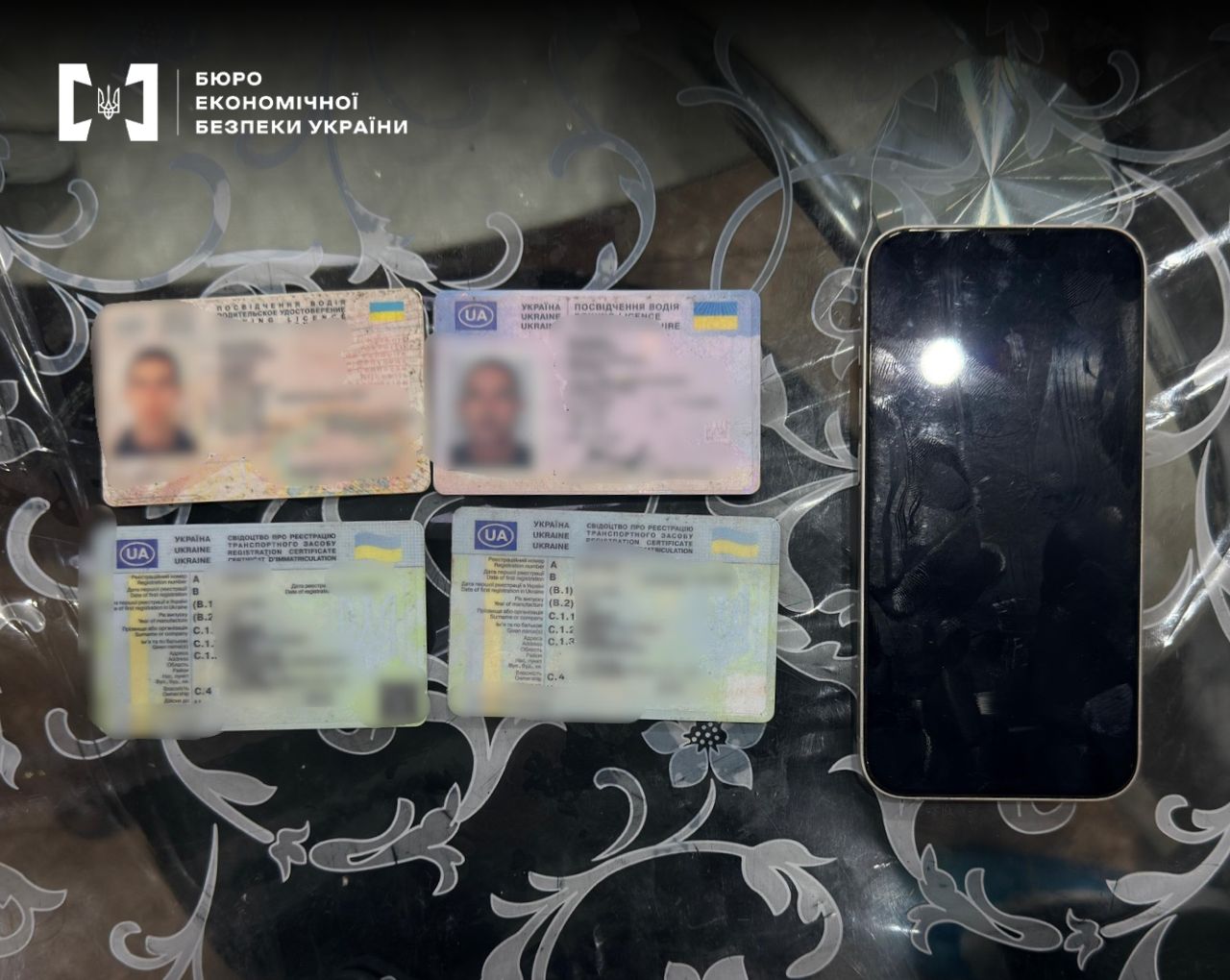 Four Ukrainian driver's licenses and a black smartphone are lying on a patterned table
