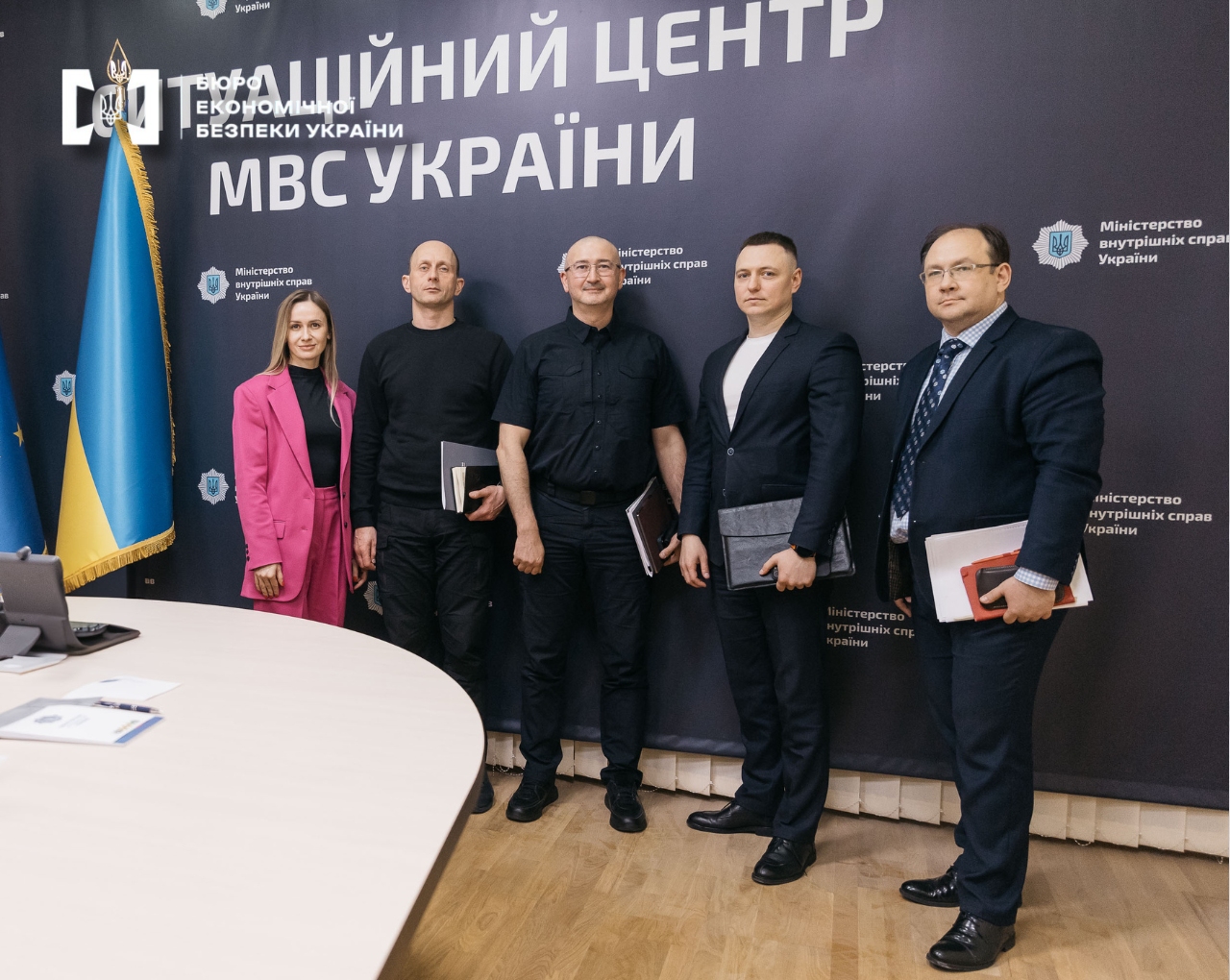 Group photo of the interagency meeting participants. The frame features four men and a woman. In the background is a banner that reads 'MIA Situation Center.' The flag of Ukraine is on the left.