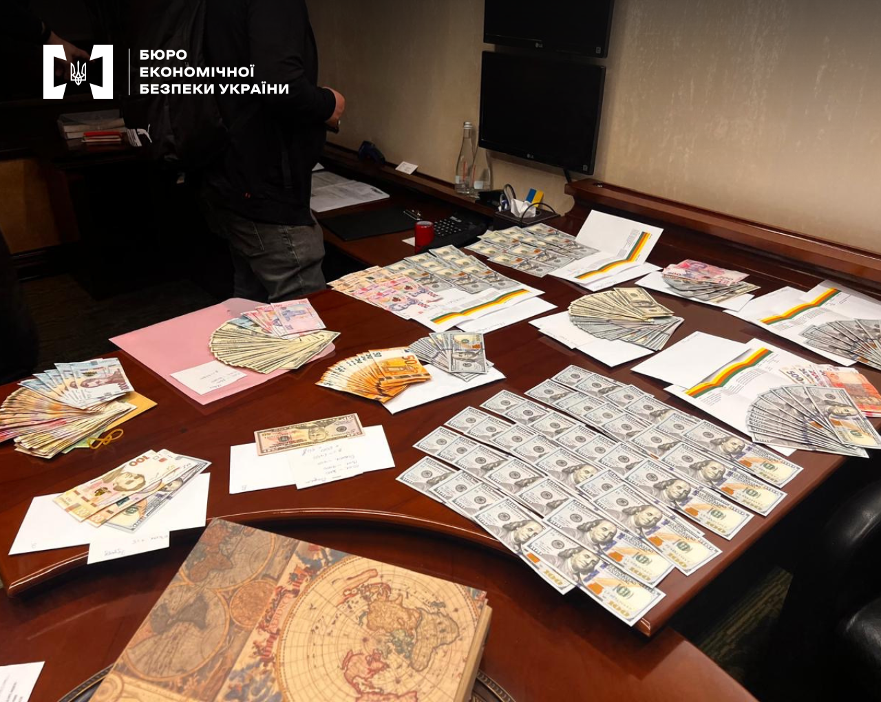 Large bundles and fanned-out stacks of US dollars, euros, and hryvnias on a large wooden table during a raid