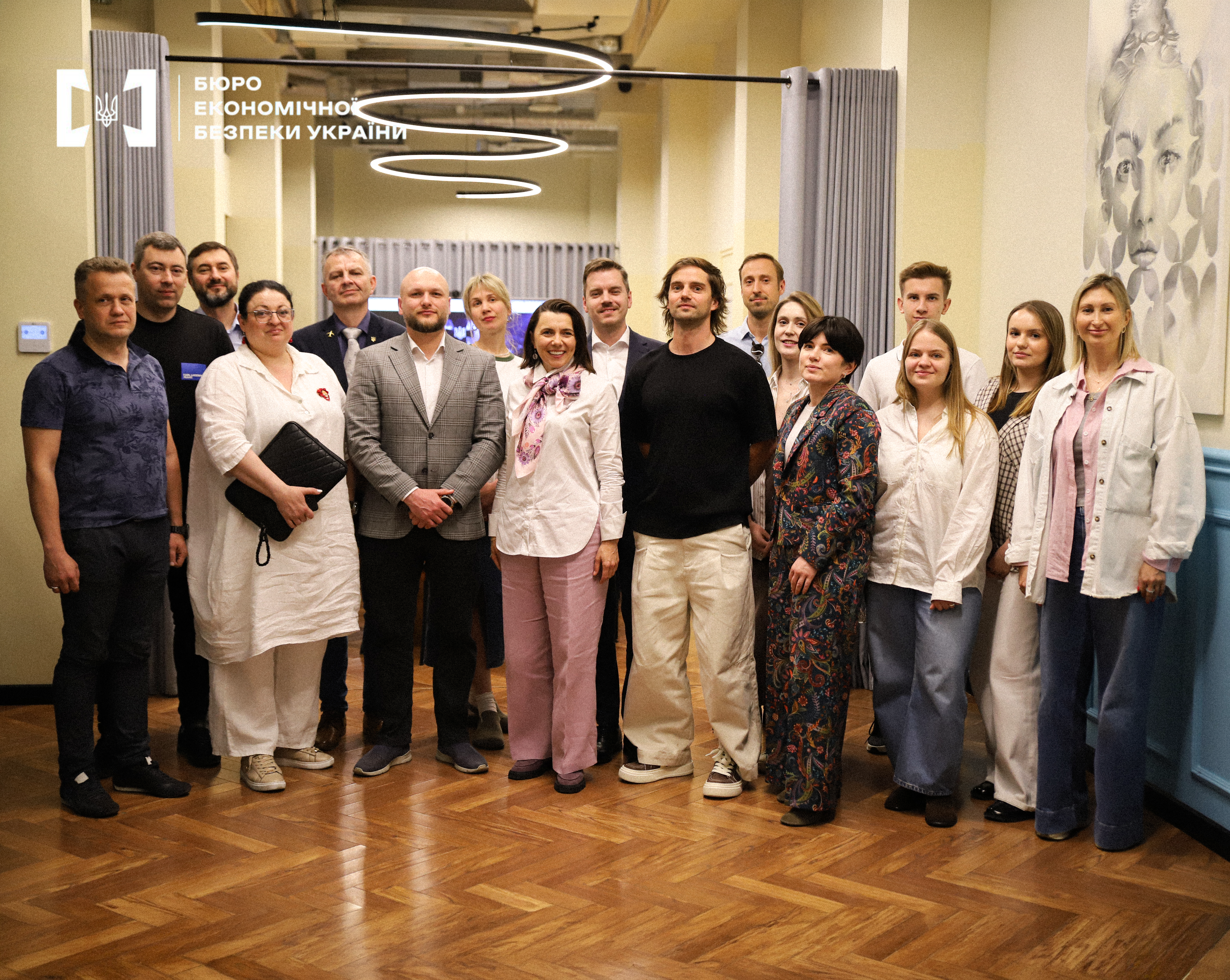 A large group of men and women in business and casual attire posing for a group photo in a bright room with a stylish spiral chandelier