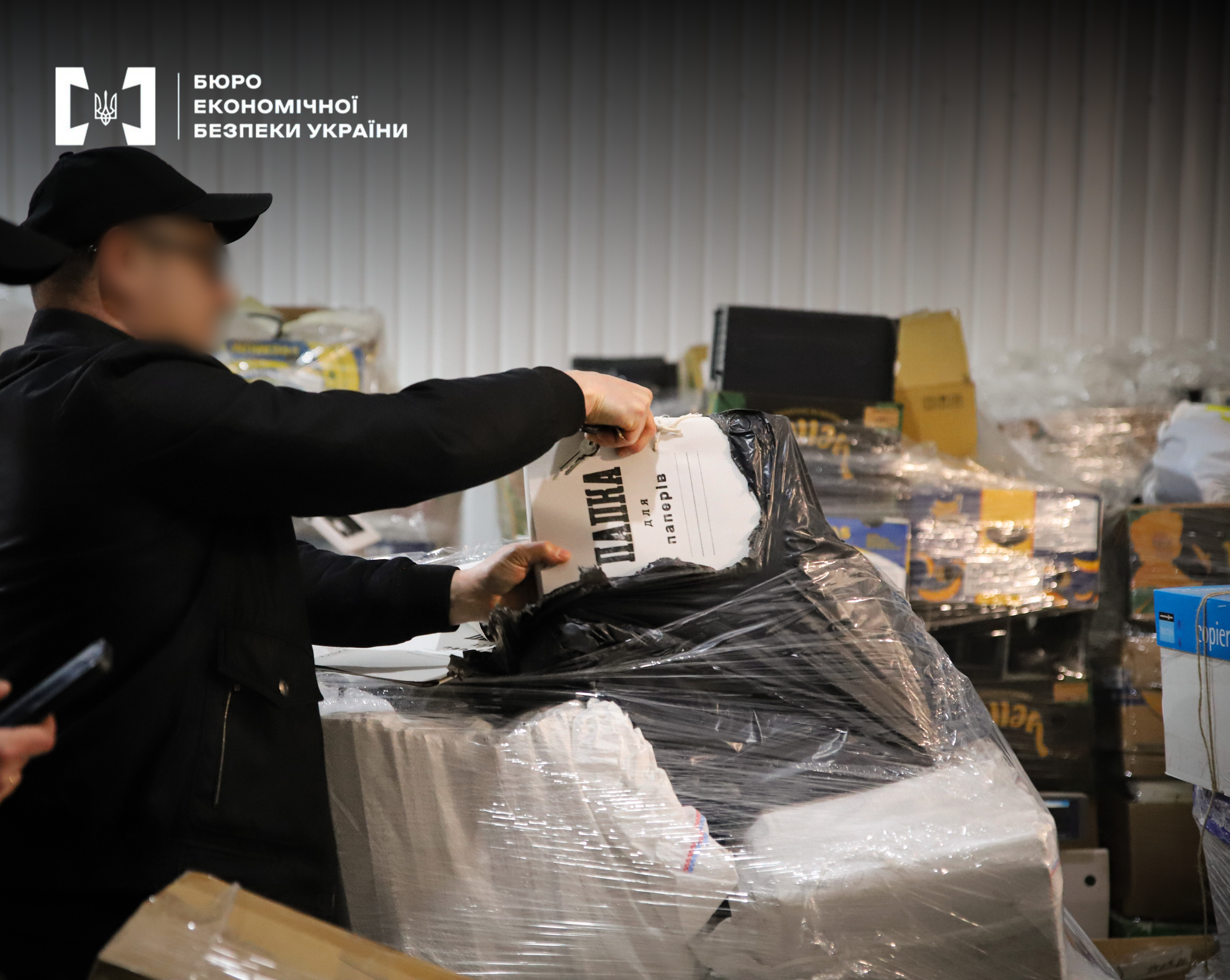 A detective of the Economic Security Bureau of Ukraine is examining seized documents and folders with papers in an office.
