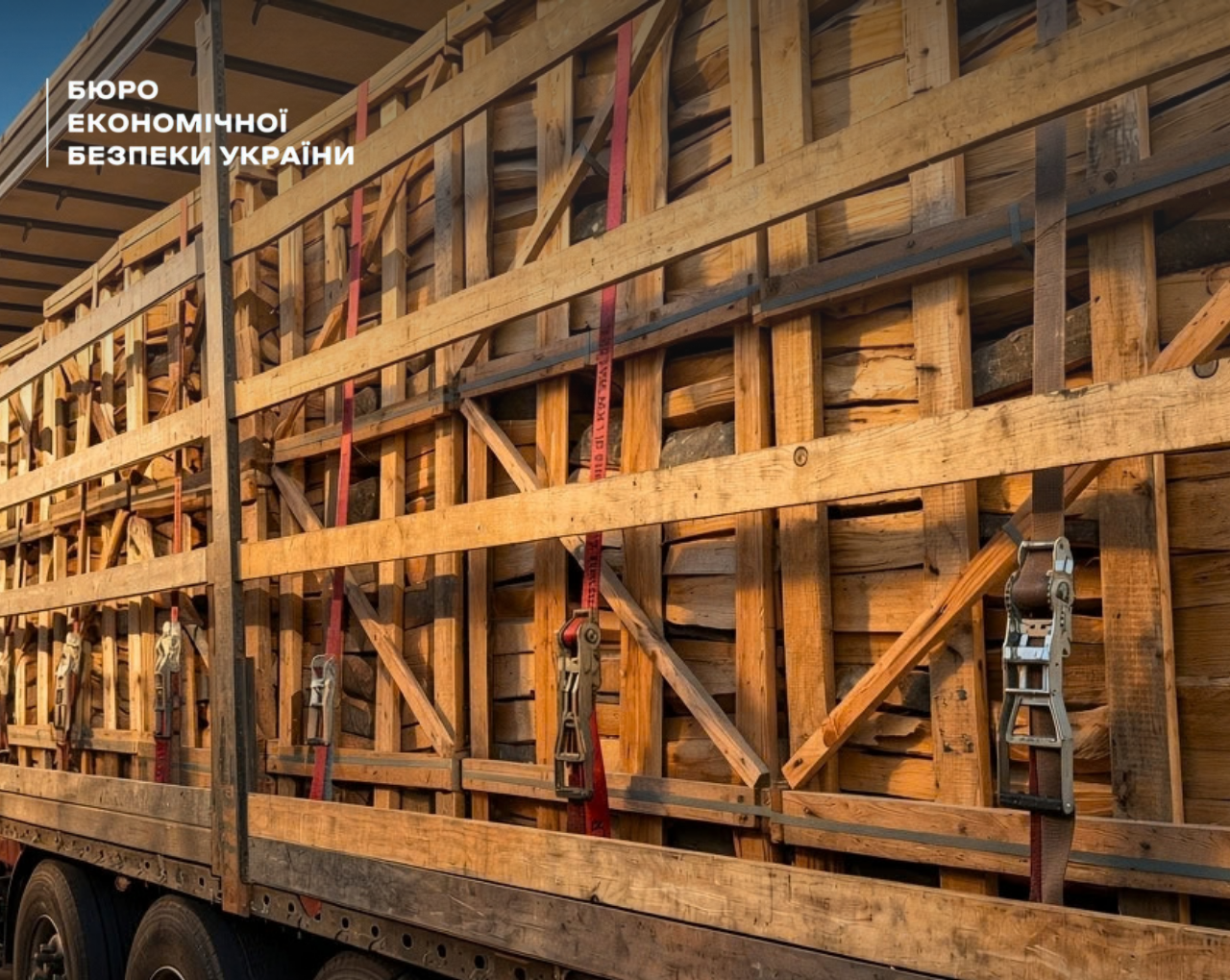 Wooden beams and boards in large wooden crates in the truck bed, secured with red and black straps.