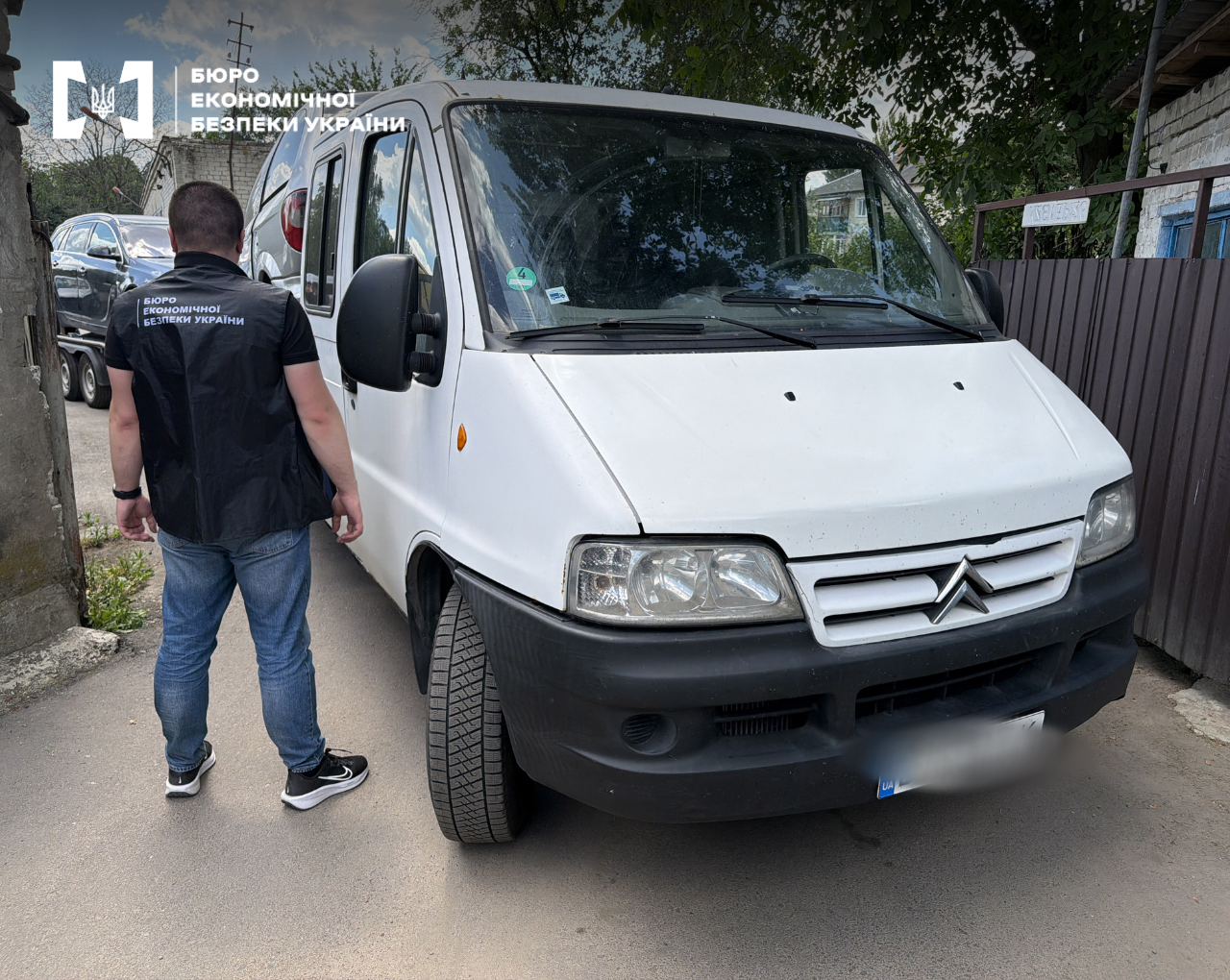 An ESBU detective stands next to a white Citroen minivan during investigative actions.