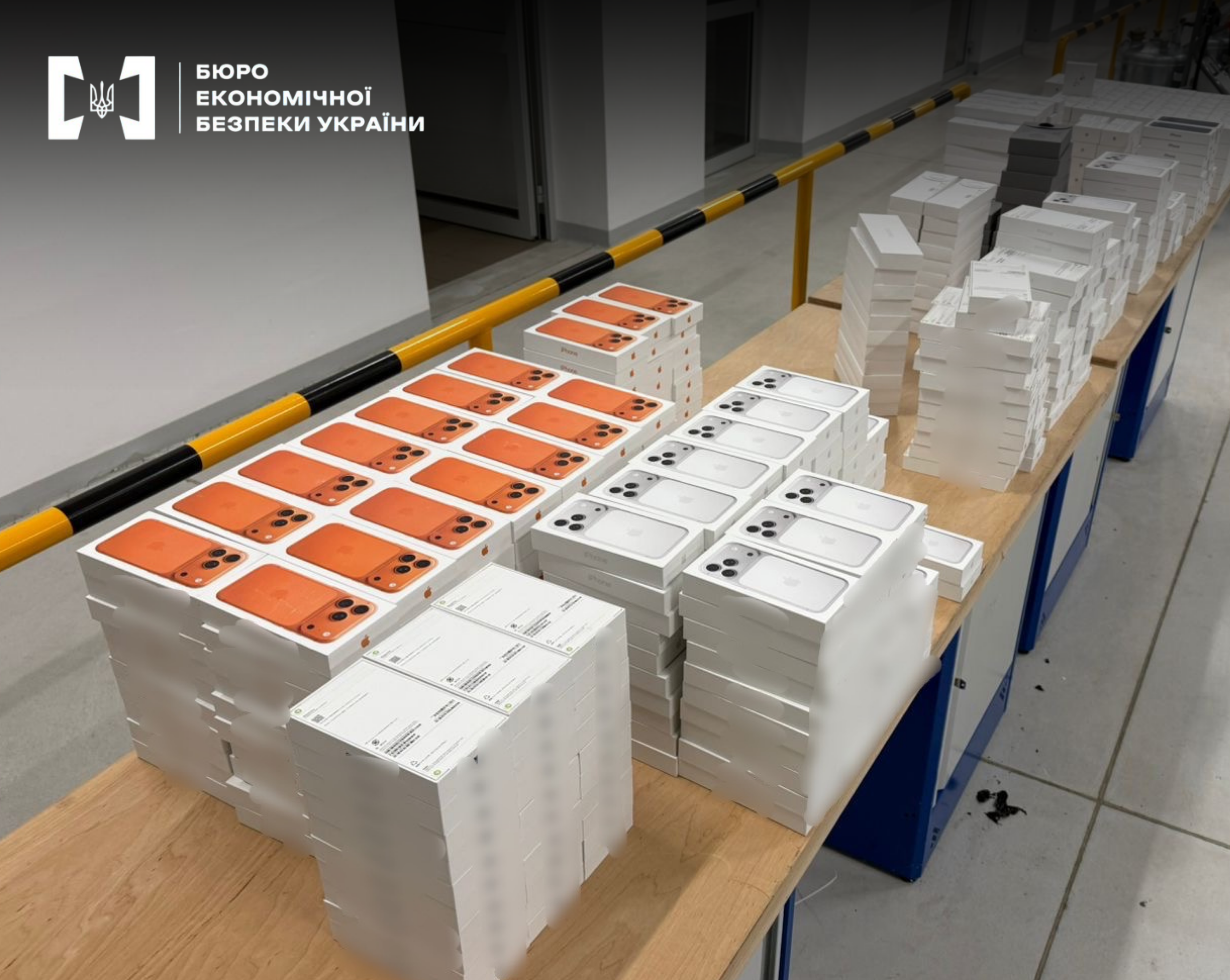 Вилучена партія смартфонів Apple у коробках, розкладена стопками на довгому столі.