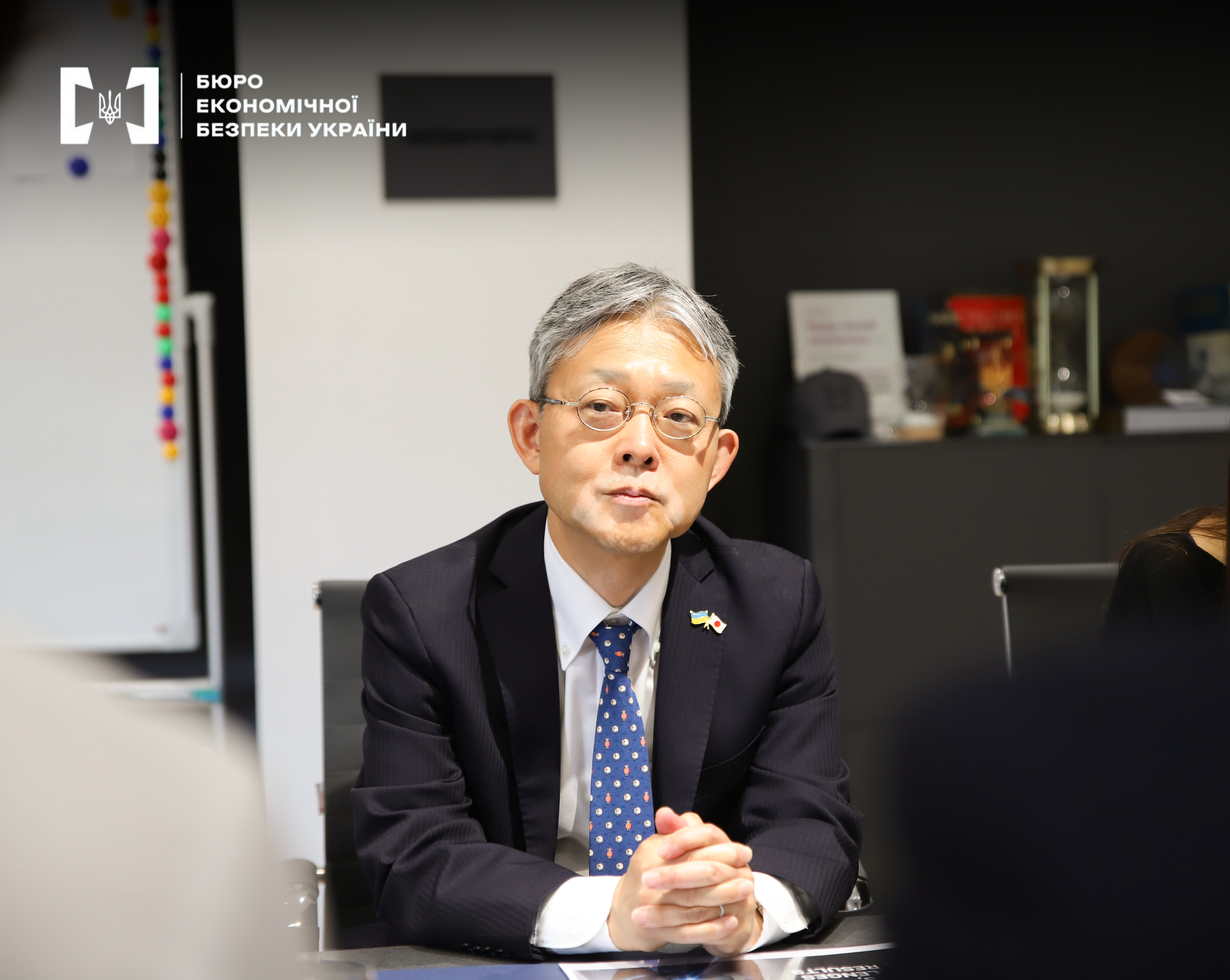 A Japanese diplomat in glasses and a suit with flags of Ukraine and Japan.