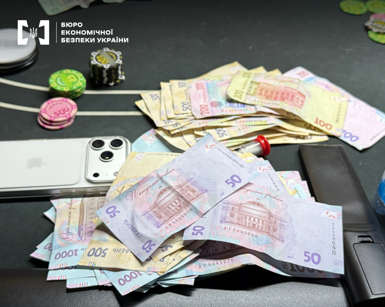 Piles of Ukrainian hryvnias of various denominations, poker chips, and a smartphone on a table.
