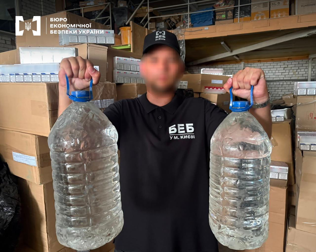 An ESBU detective holds two large plastic carboys with transparent liquid against the background of a warehouse with boxes of cigarettes.