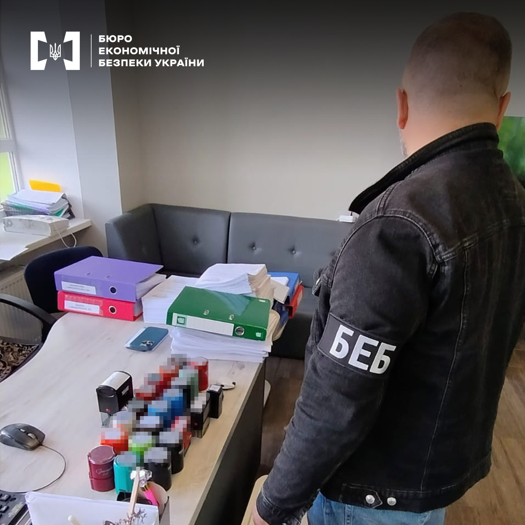 Детектив БЕБ проводить обшук в офісі. На столі велика кількість печаток, документи в теках і без, смартфон.