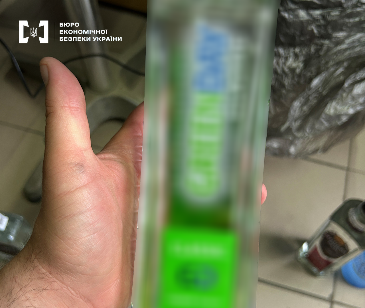 A hand holding a blurry glass bottle of vodka with a green label