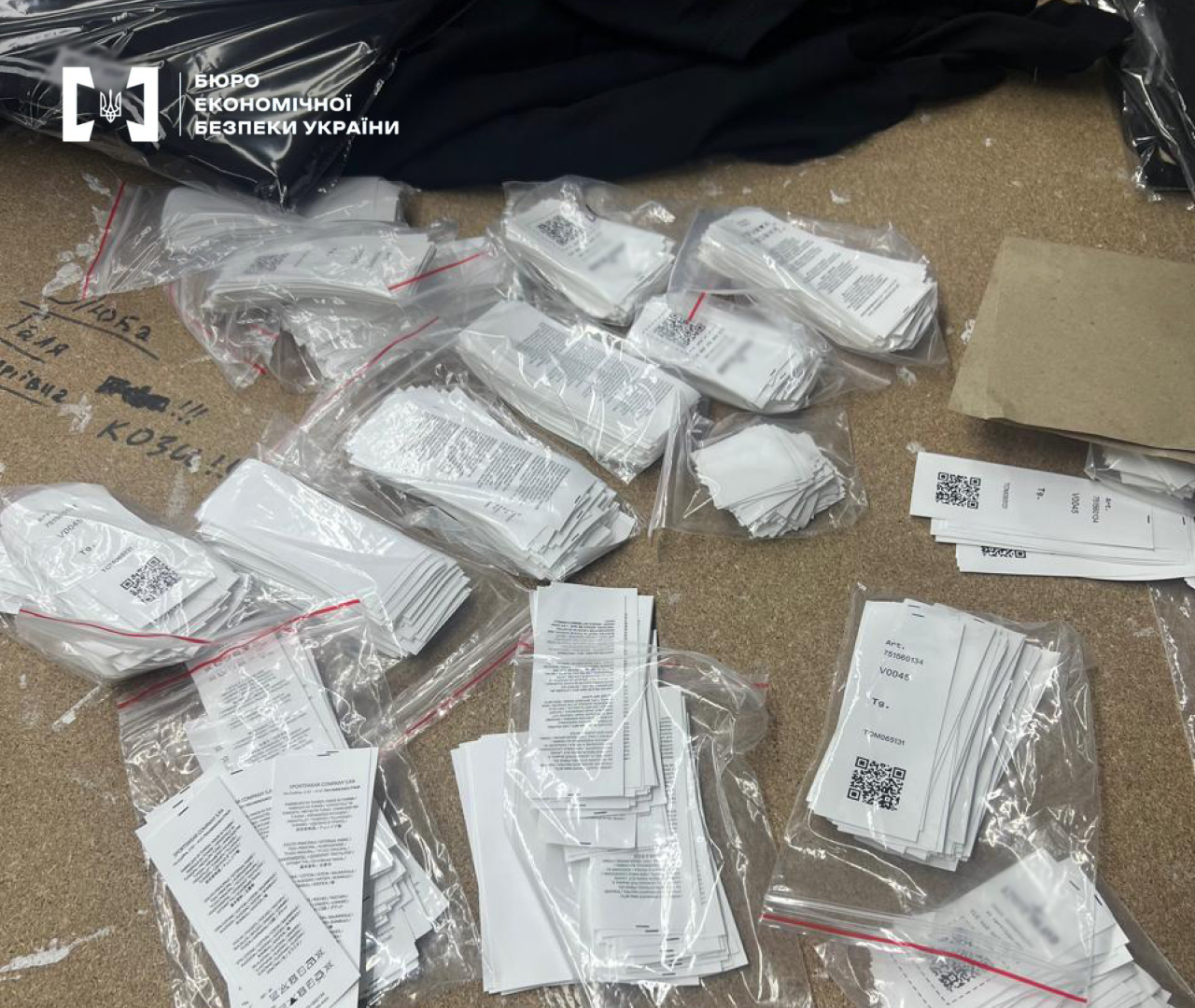 A batch of seized white clothing tags, labels, and price tags with QR codes in plastic bags and stacks during investigative actions.