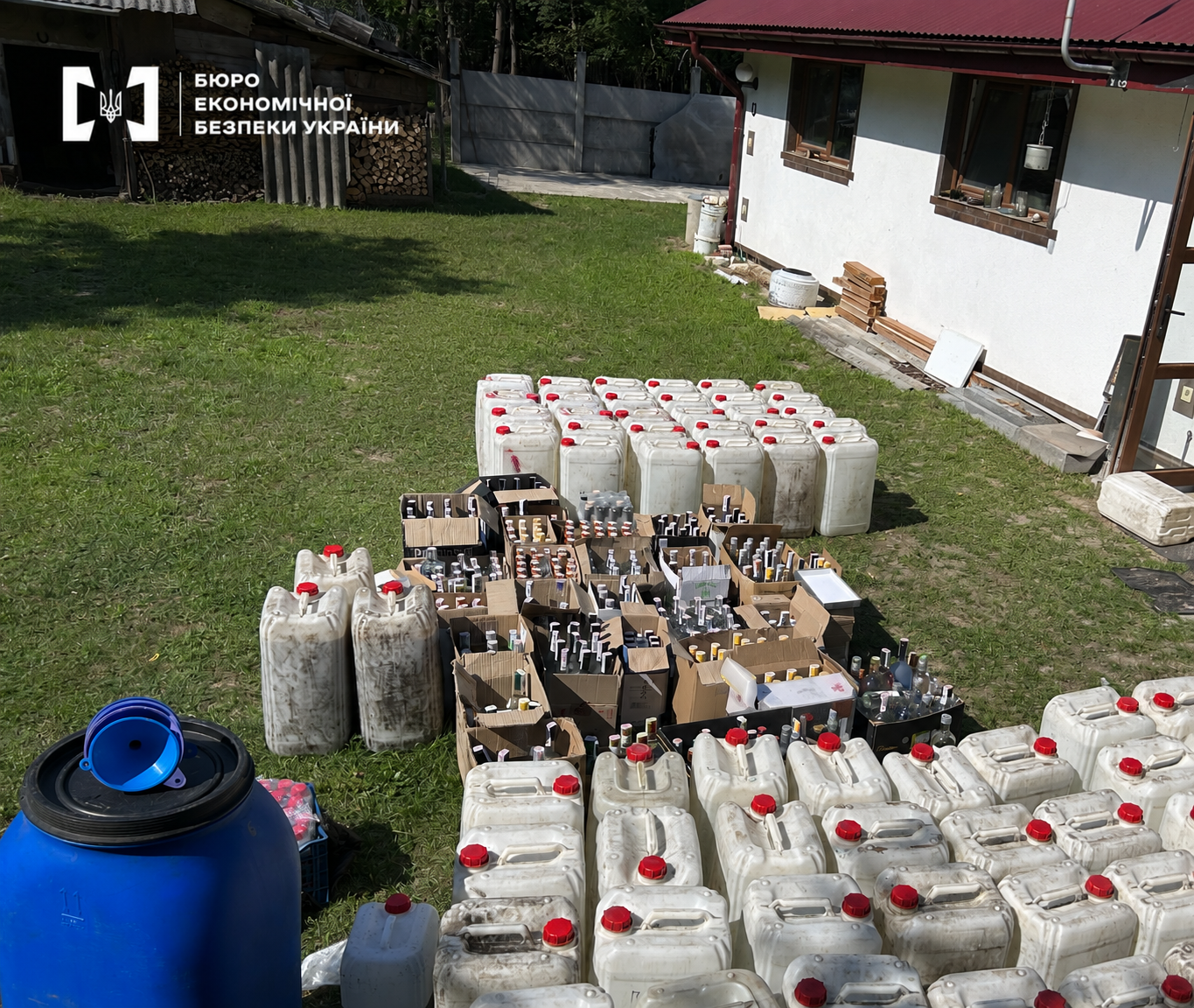 Large stacks of white canisters and boxes with bottles of alcohol on the grass near the house