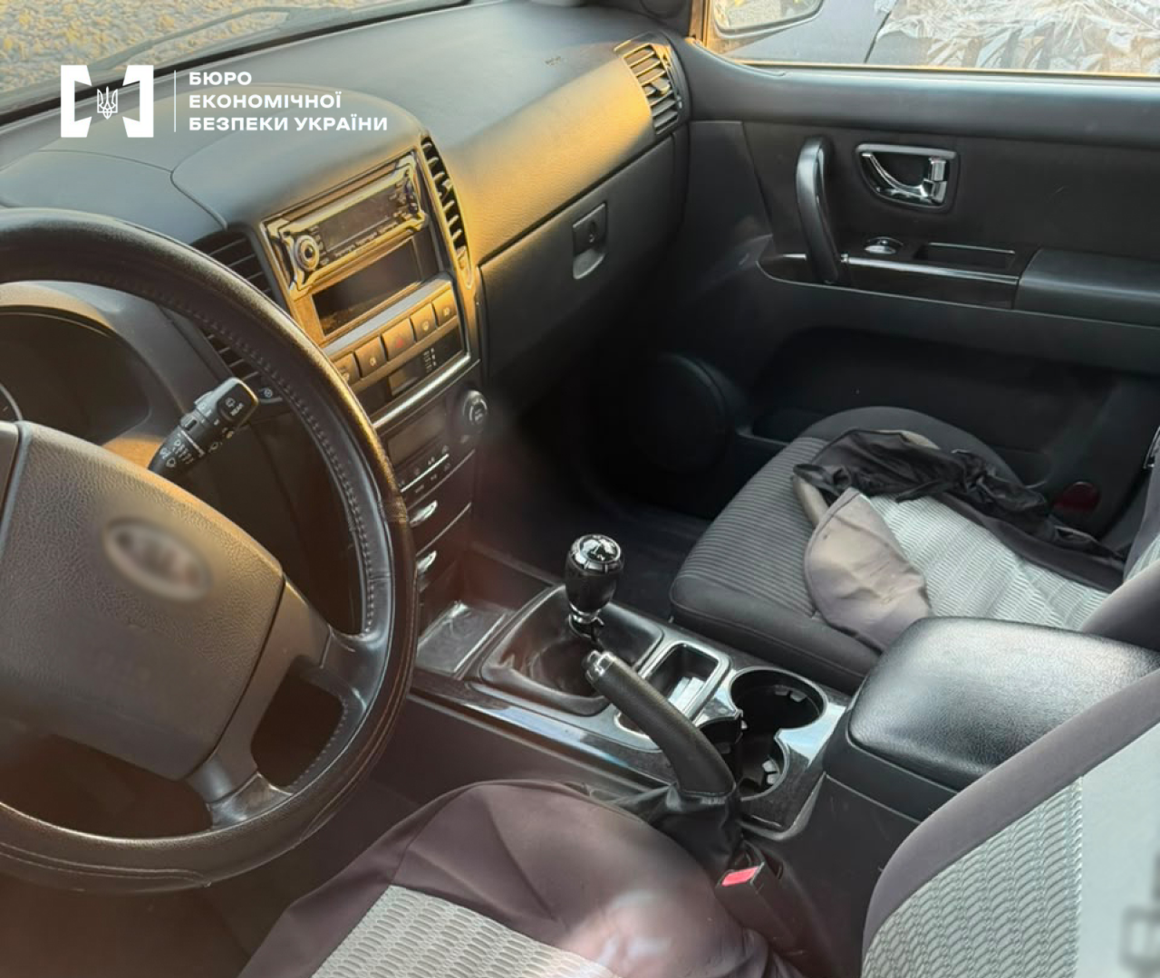 A black leather steering wheel, dashboard, and driver's seat of a car with scattered items.
