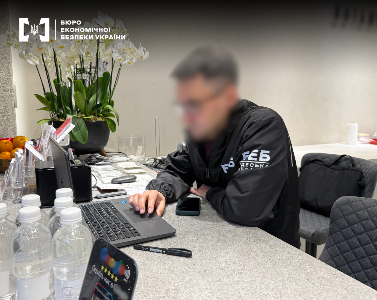 A ESBU detective sits at a desk near a computer and water bottles
