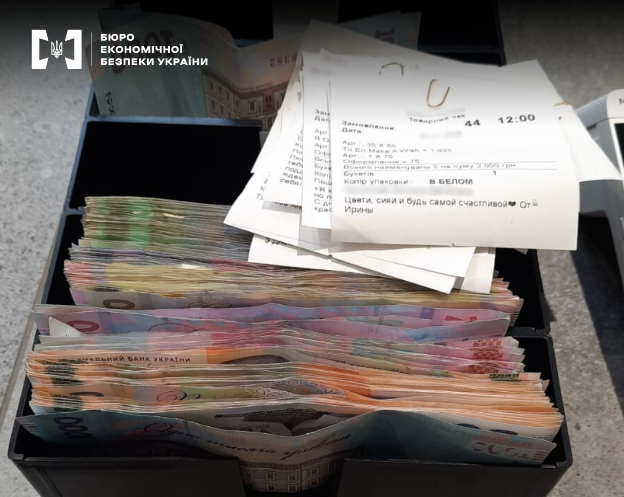 Money of various denominations in a black tray next to paper store receipts.