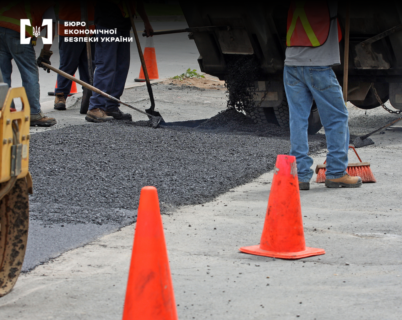 Road workers laying new asphalt using specialized machinery, with orange cones in the foreground.