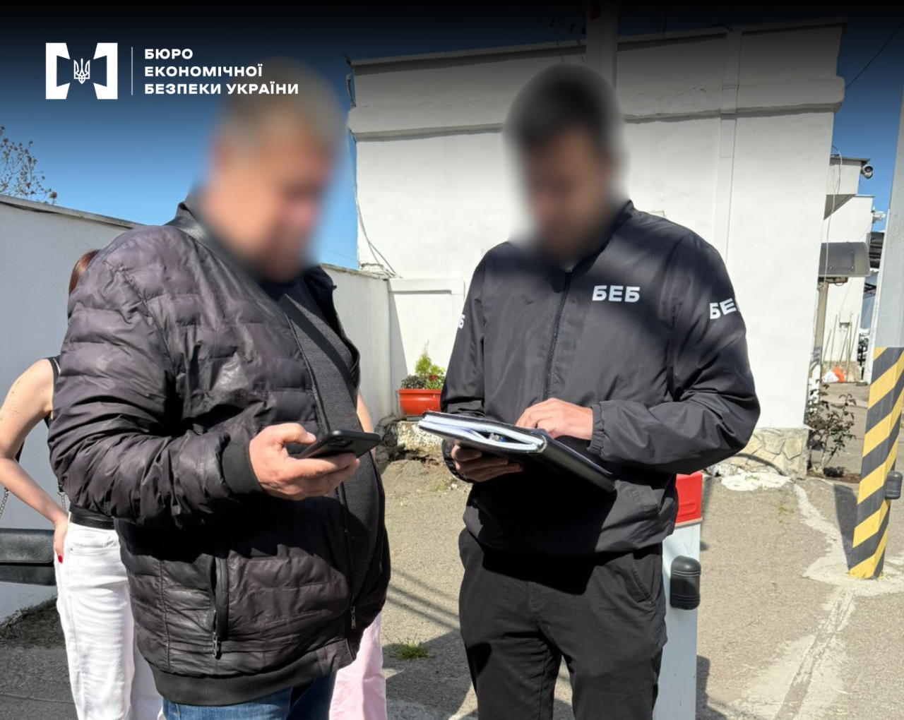 An ESBU detective takes notes in a folder while talking to a man on the street. The people's faces are blurred.