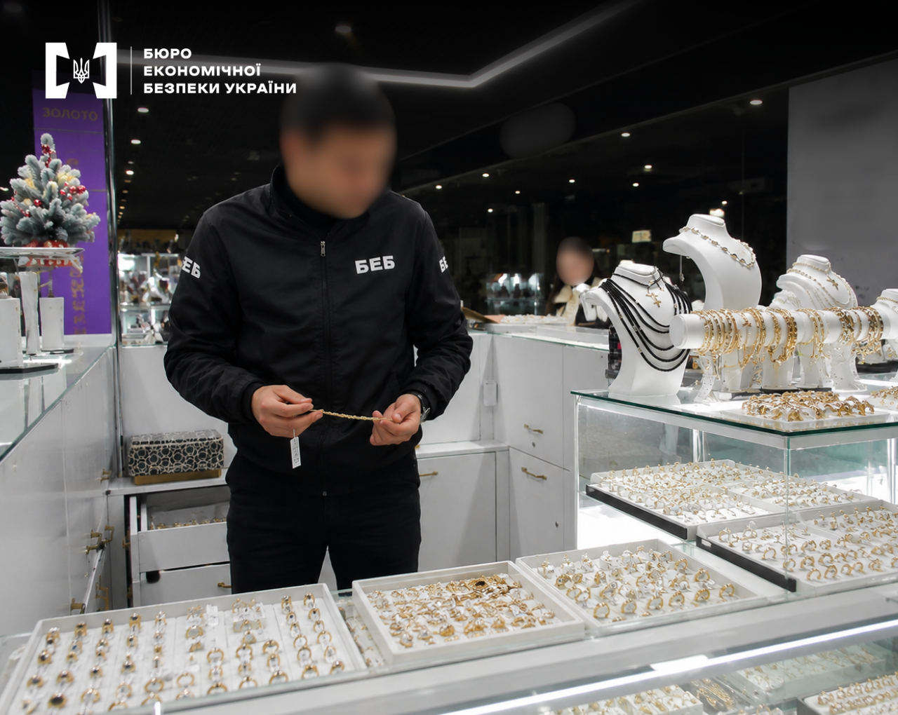 An ESBU detective examines a piece of gold jewelry in a jewelry store with window displays
