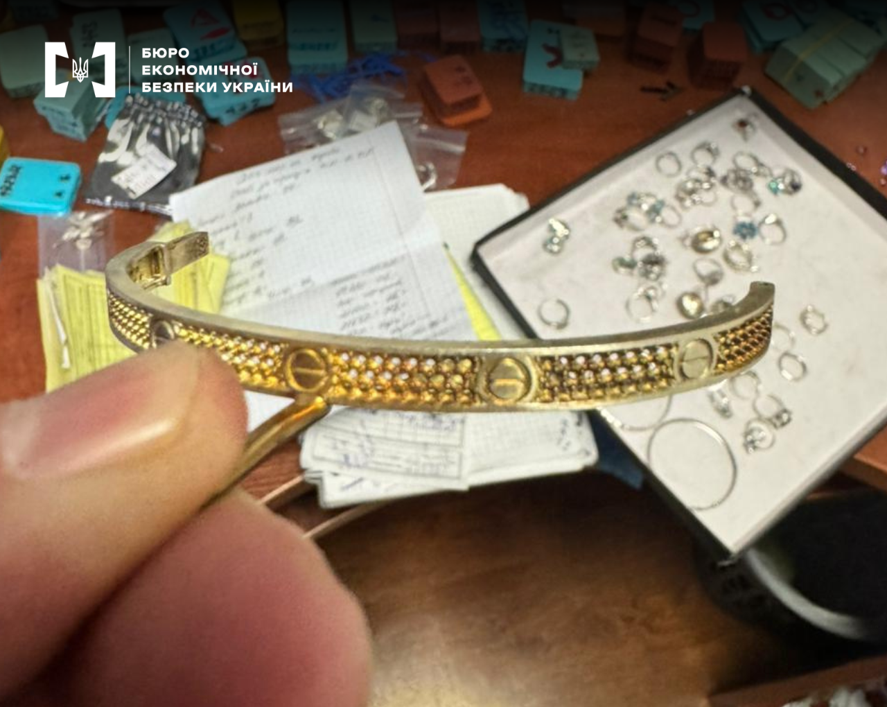 A gold bracelet in a hand against the background of a table with documents and other jewelry