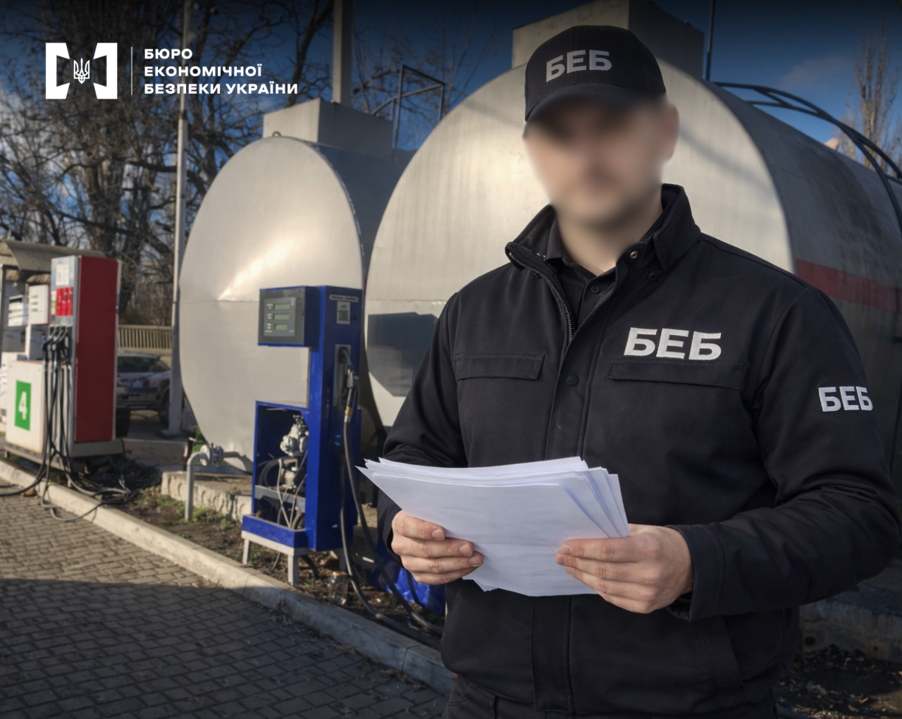 An ESBU detective holding documents against the background of a gas station and fuel storage tanks