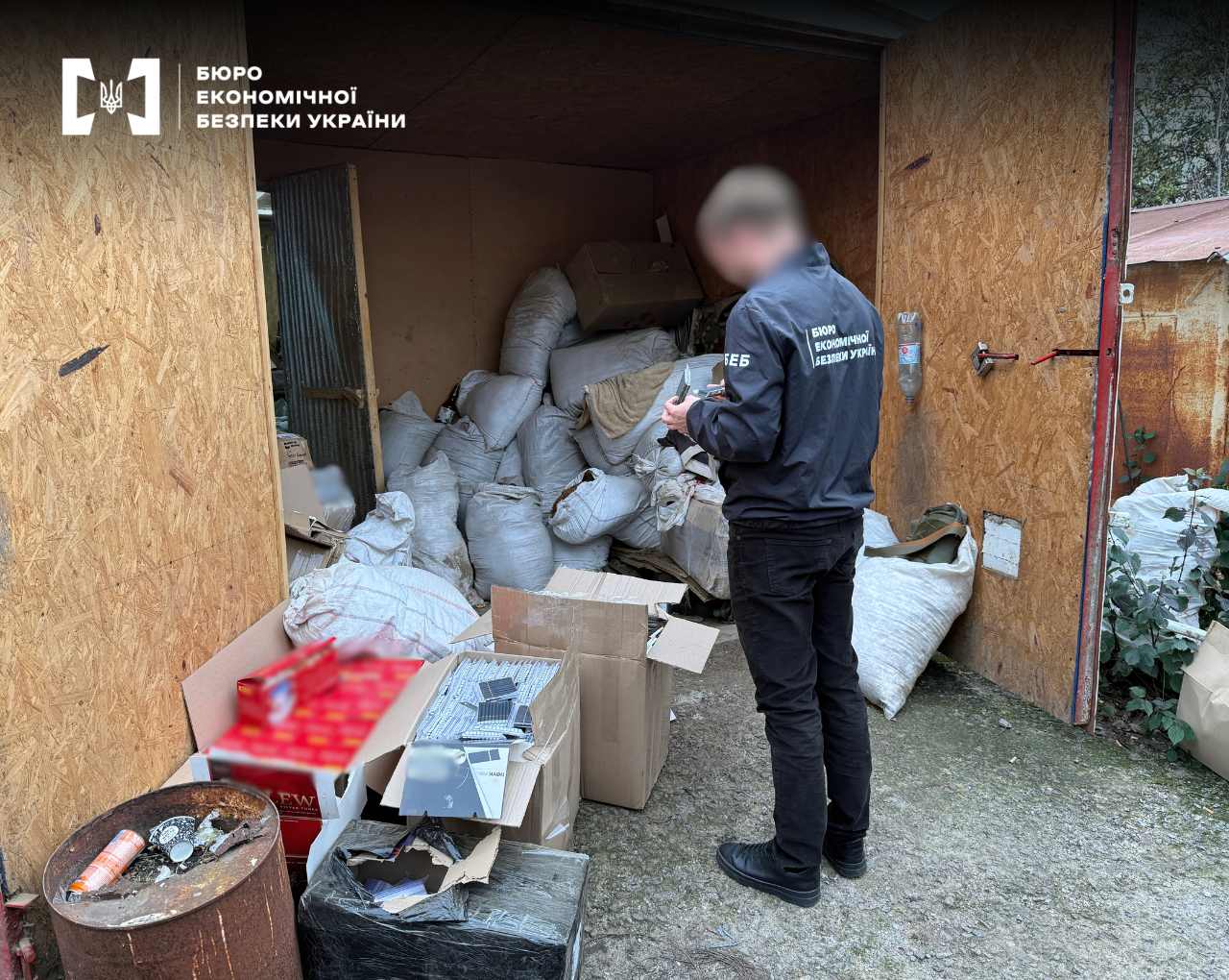 An ESBU detective inspects a discovered warehouse containing a large number of sacks and cardboard boxes filled with products.