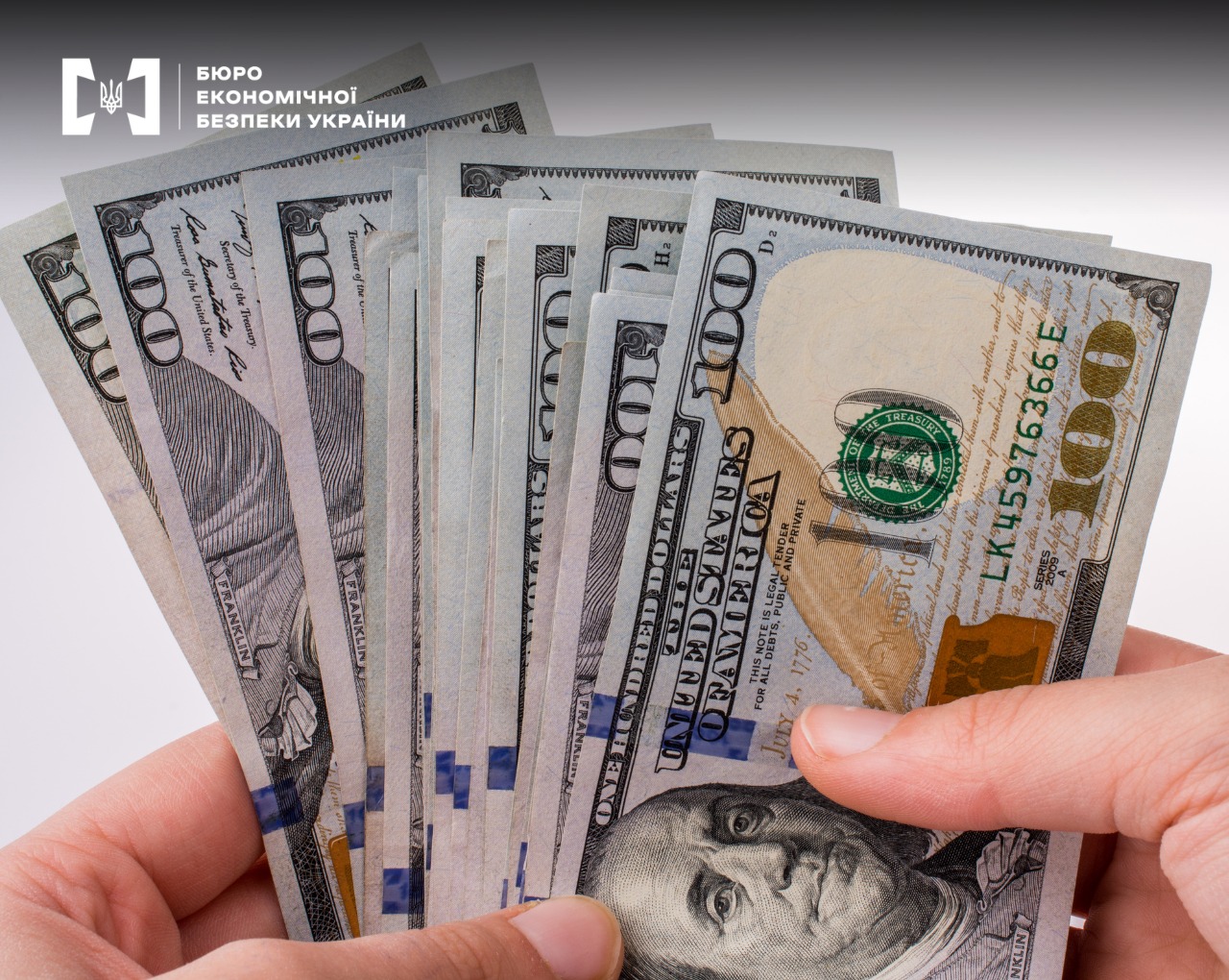 Close-up of hundred-dollar bills in hands, with the ESBU emblem in the upper corner.