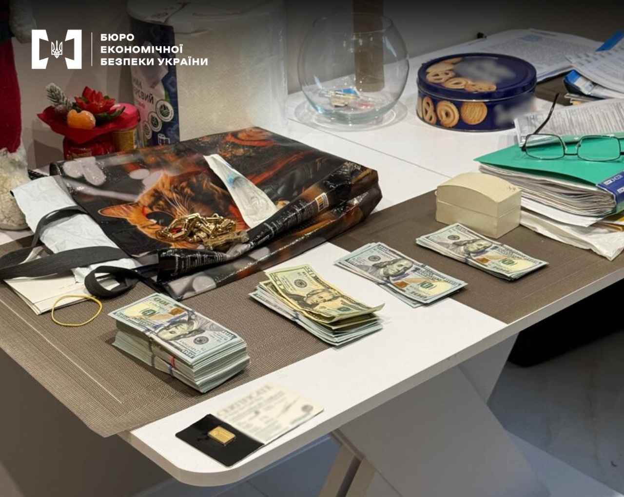 Physical evidence during the investigation: stacks of US dollars, gold jewelry, and documents laid out on a white table during a search