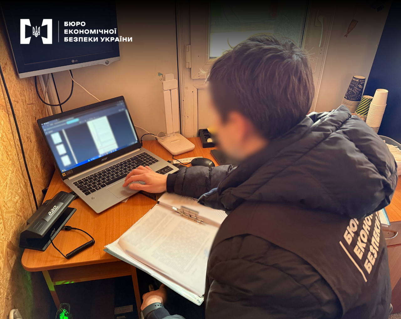 Investigative actions. An ESBU detective reviews data on a laptop and works with documents inside a gas station office.