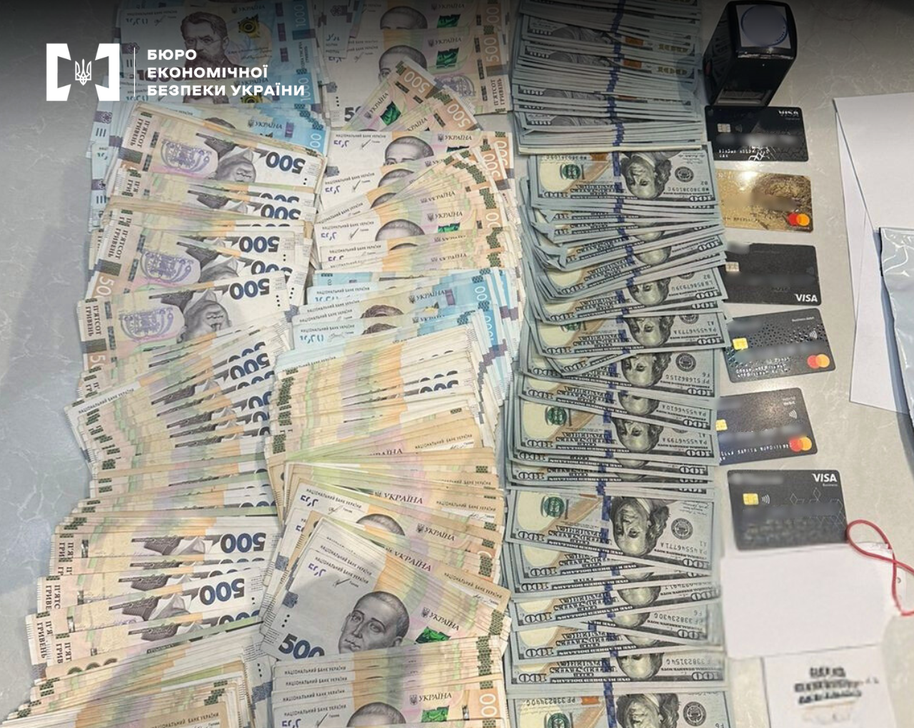 Large sums of cash are laid out, including 500 hryvnia and 100 US dollar bills, along with six bank cards from various payment systems (Visa, Mastercard) and a black seal