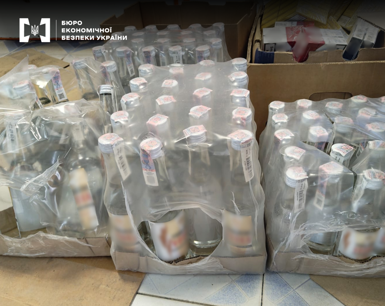 Bottles of strong alcohol with excise stamps in shrink-wrap packs against the background of cardboard boxes with cigarettes.