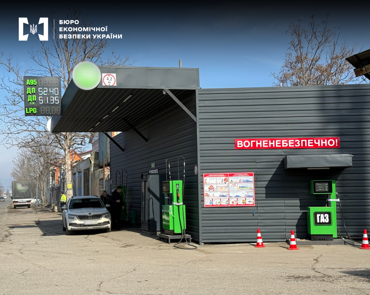 Two modern, bright green fuel dispensing units are installed under a canopy, with two red-and-white traffic cones placed in front of the facility.