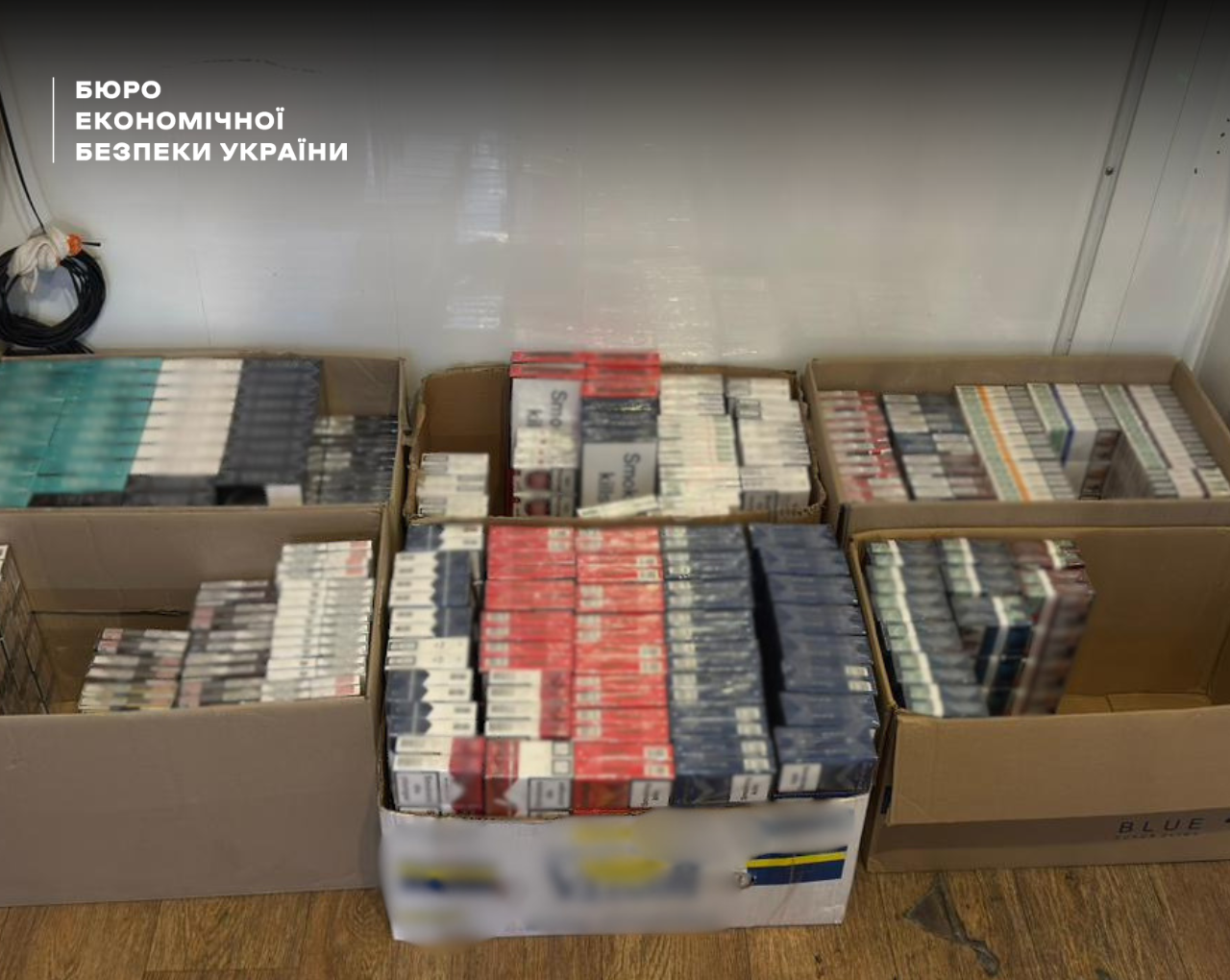 Stacks of red, blue, and grey cigarette packs without excise stamps in open boxes on the floor.