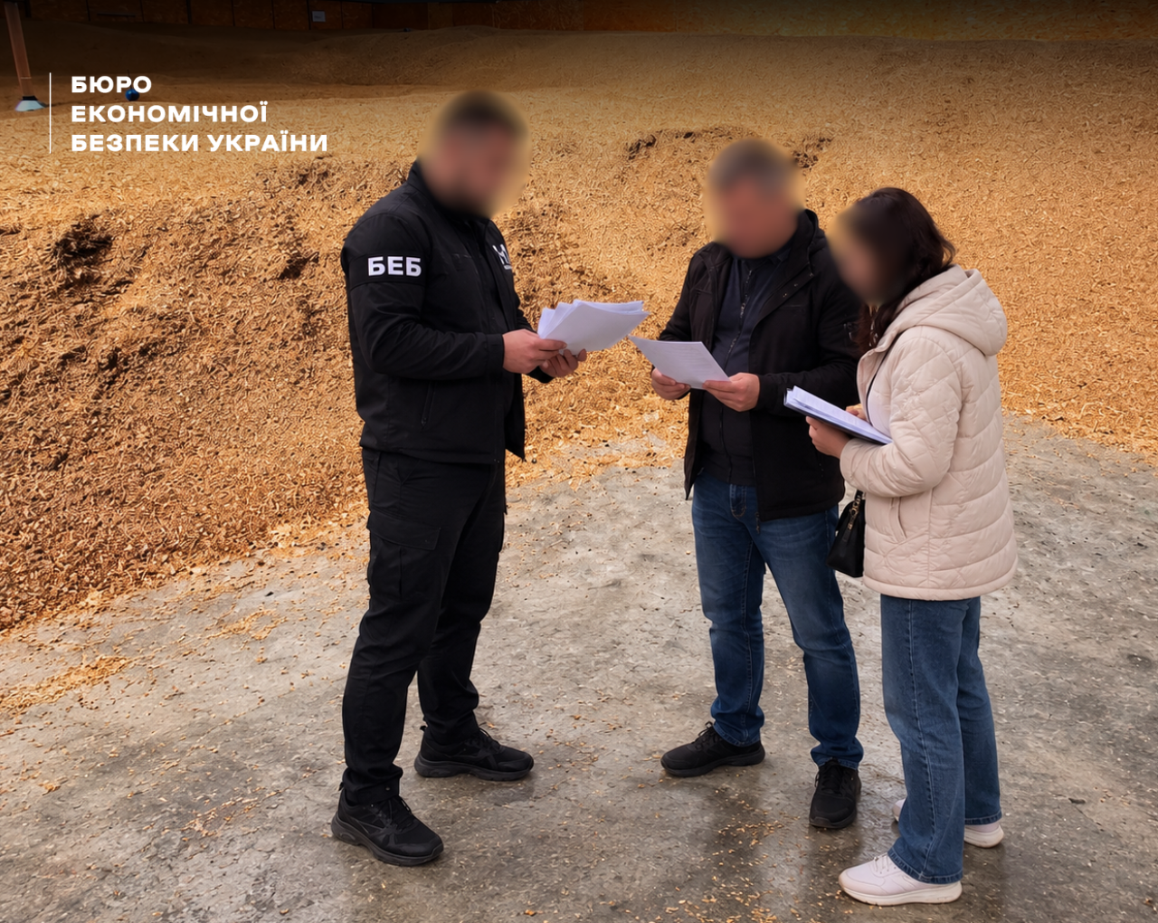 An ESBU detective and two citizens holding documents stand on an open-air yard filled with timber and wood chips