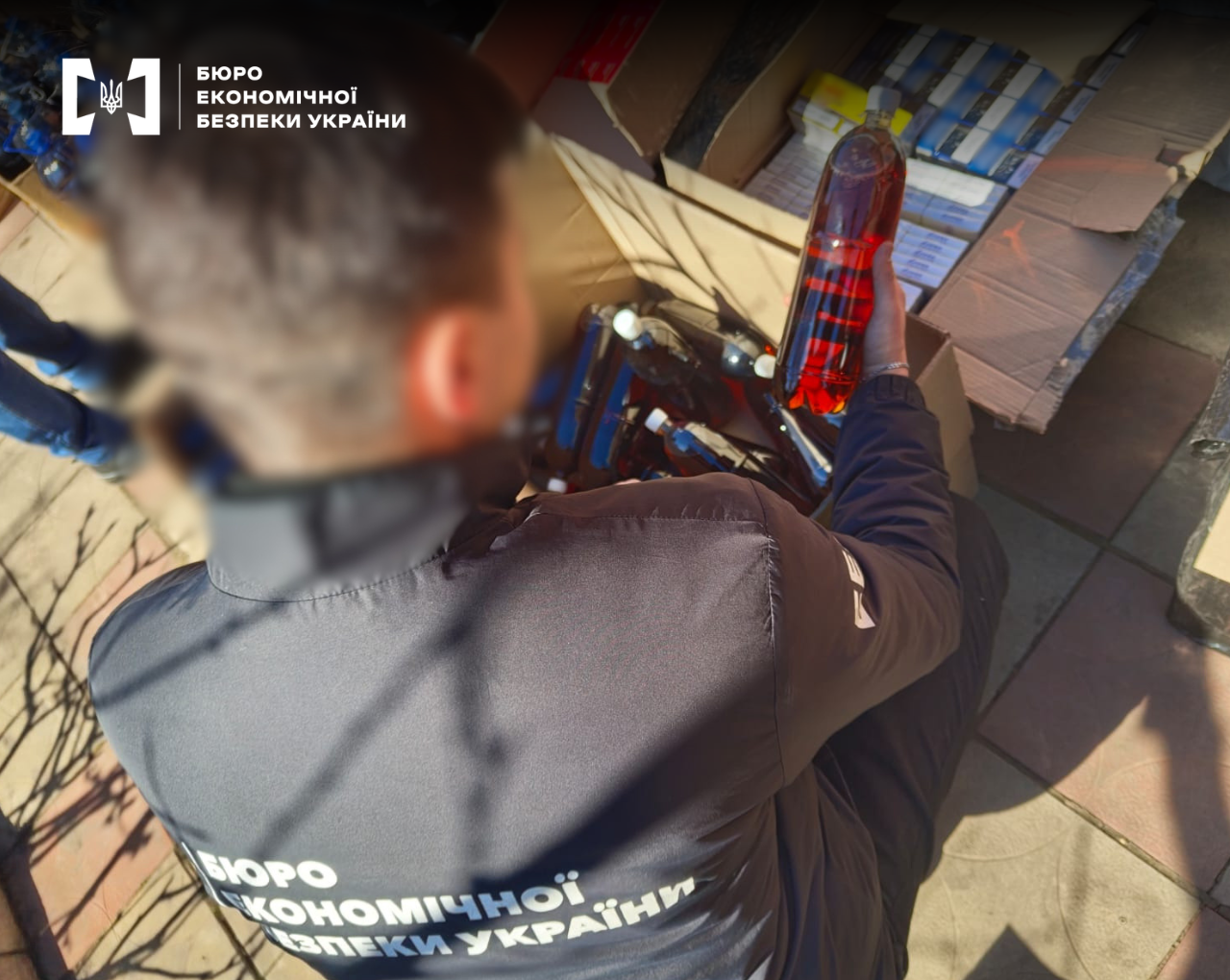 An ESBU detective holds a bottle filled with dark liquid over cardboard boxes of cigarettes.