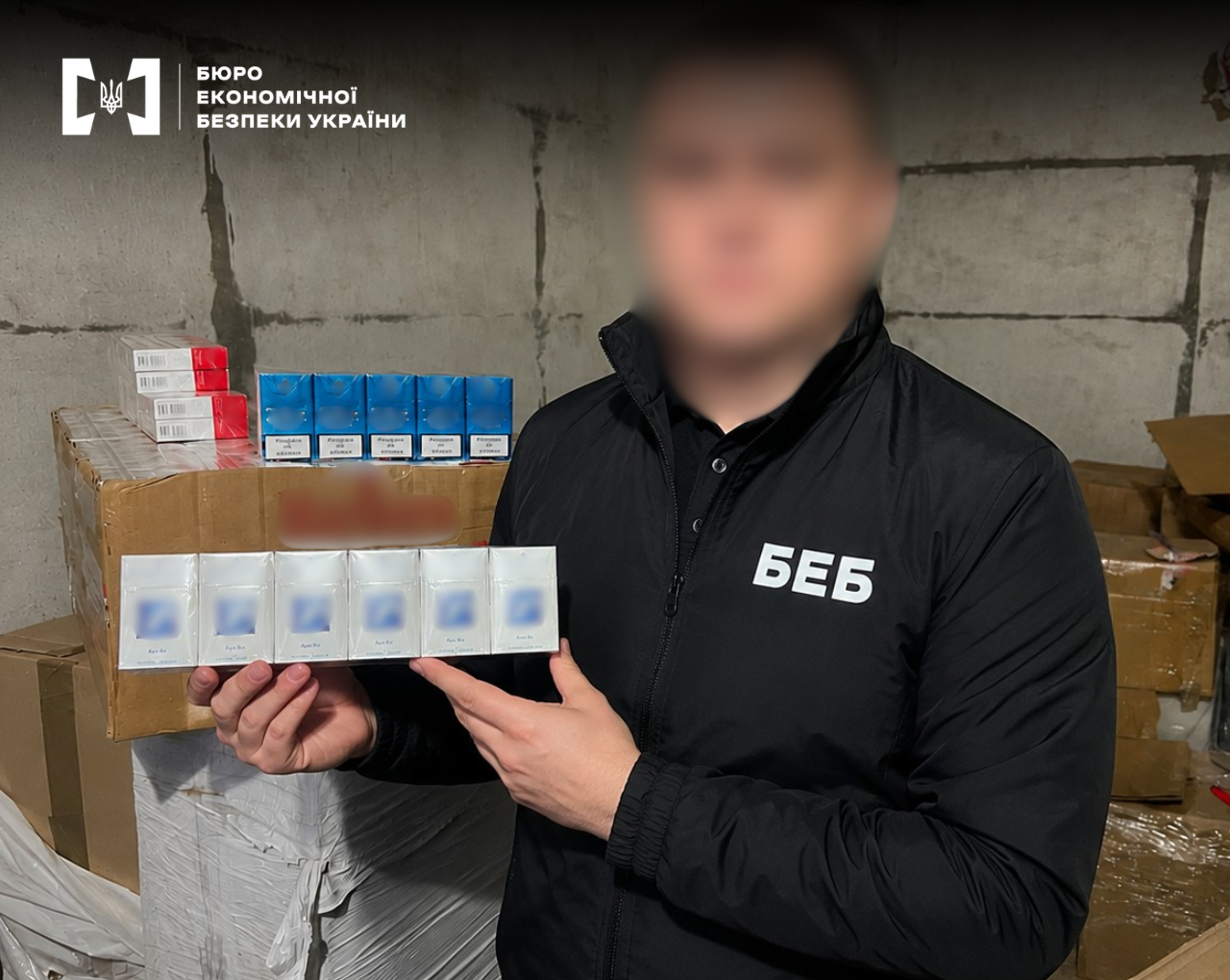 A ESBU detective holds packs of counterfeit tobacco against the background of boxes of goods