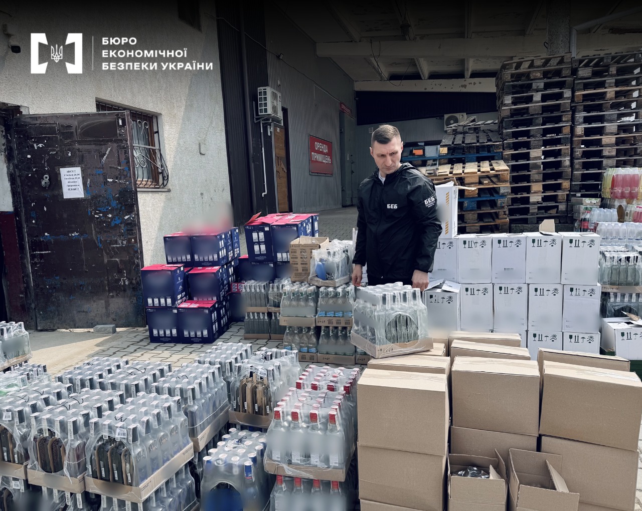 A ESBU detective among hundreds of alcohol bottles and cardboard boxes during a search of an underground workshop.